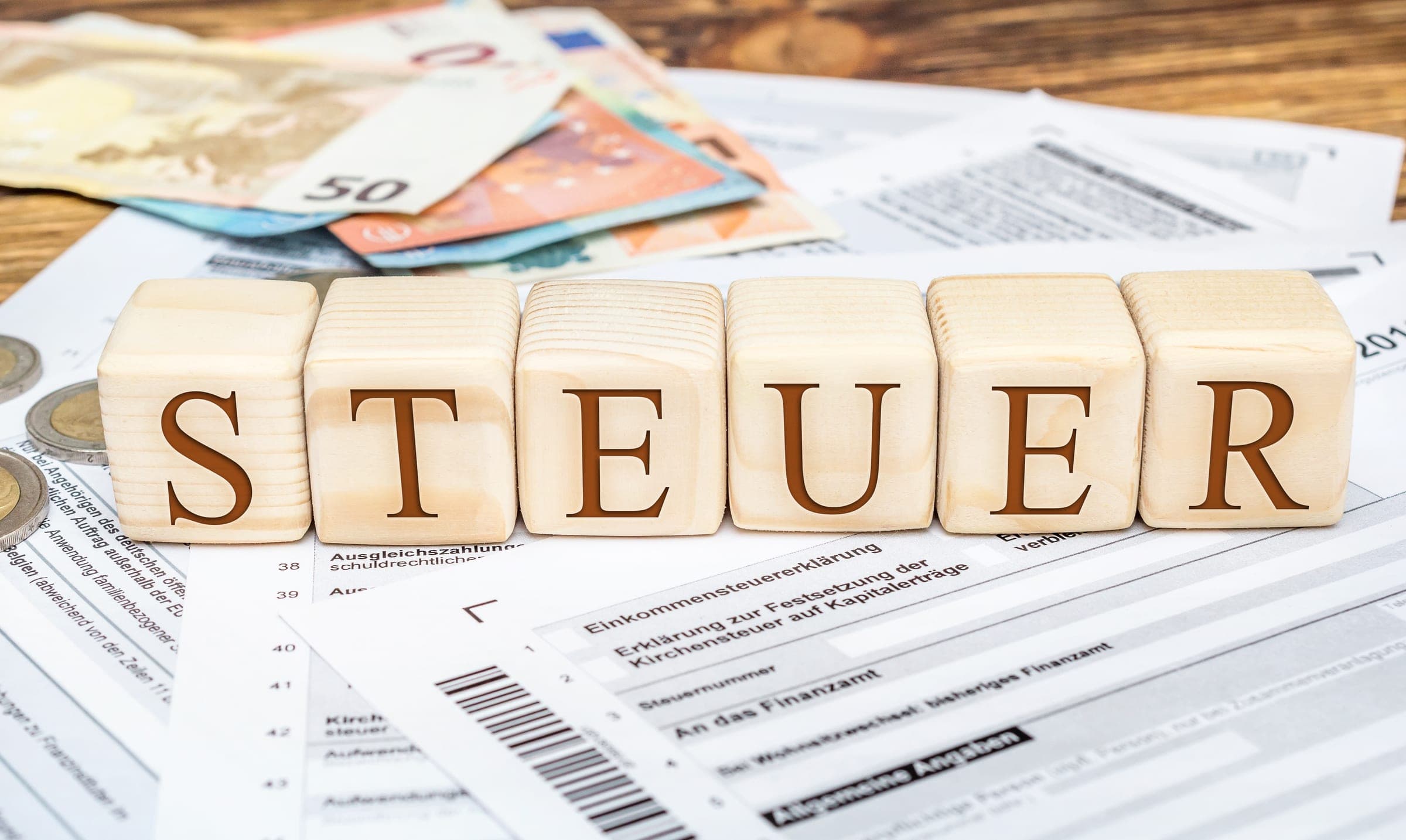 Blocks spell 'Steuer' over currency documents, representing certificate of currency topic.
