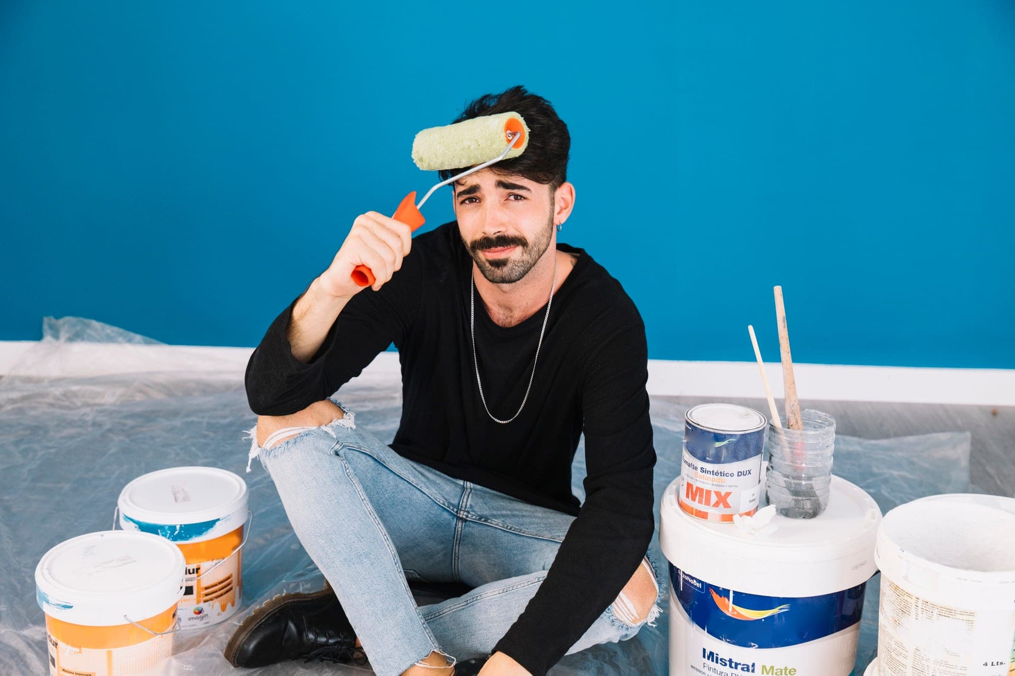 Painter sitting with paint cans and roller in a blue room, highlighting contractors' insurance needs.