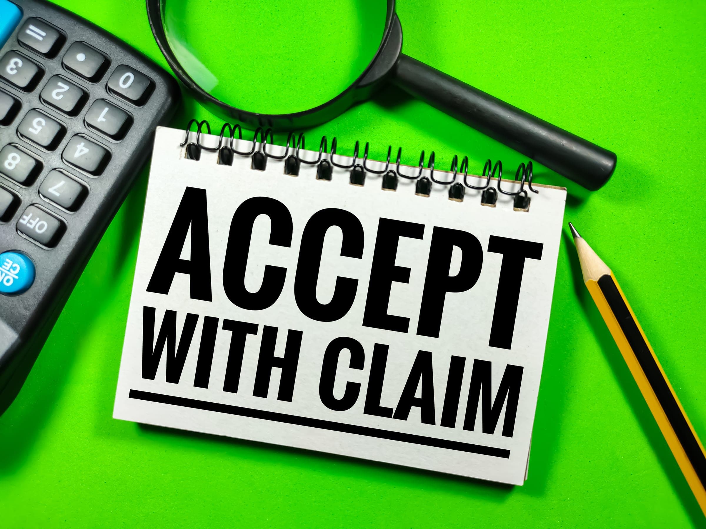 Notebook with 'Accept with Claim' beside calculator and magnifying glass on green surface.