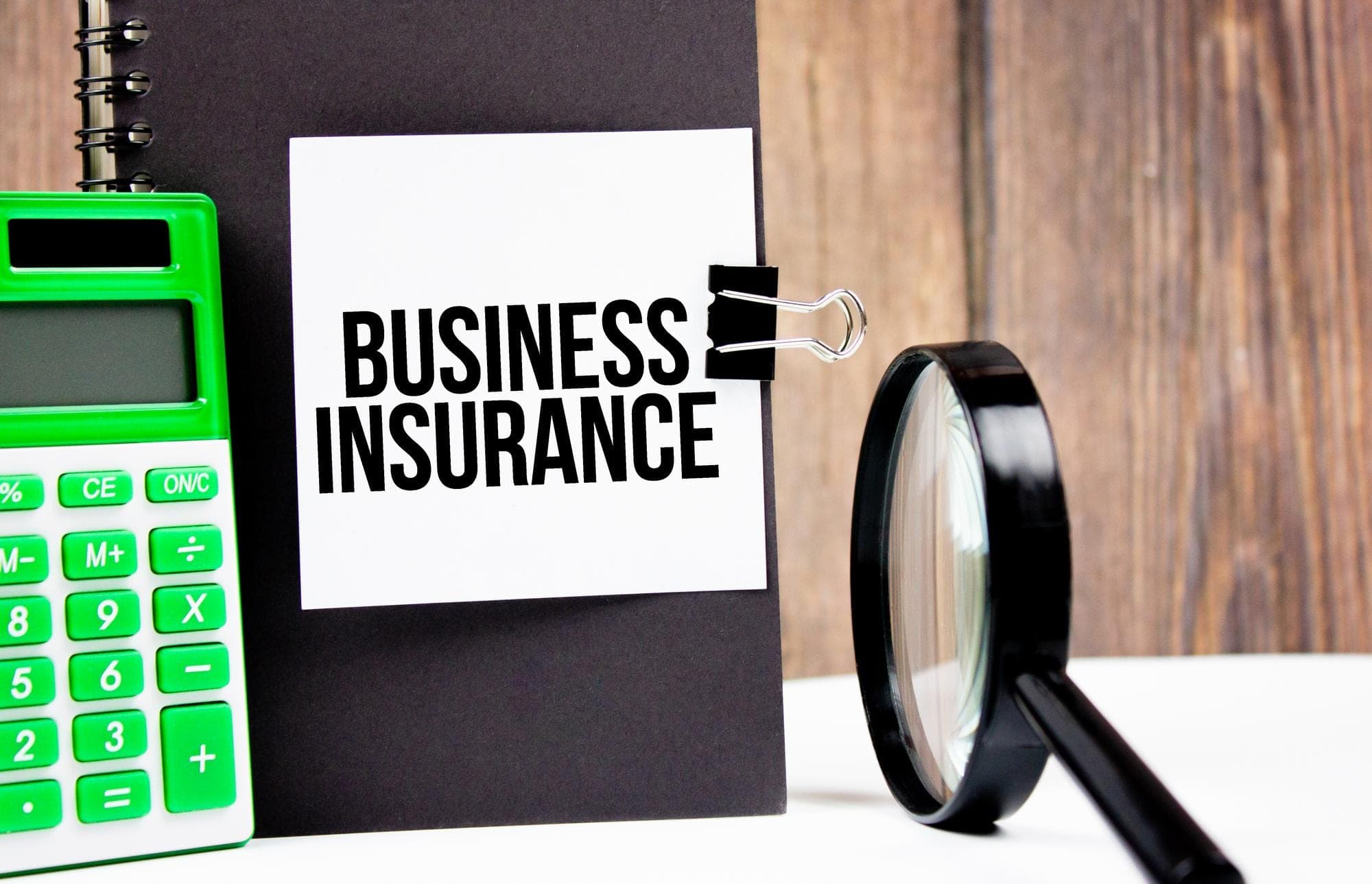 Calculator and magnifier next to business insurance sign on clipboard.